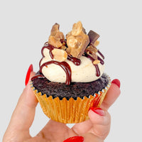 A hand with long red nails holds the $100 JRC Gift Bag from Jenna Rae Cakes against a plain light grey background.