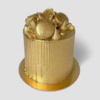 A cake decorated with Jenna Rae Cakes’ Antique Gold Edible Lustre Dust (5g shaker, pack of 6): gold fondant, gold drip, assorted gold sweets and meringues on a gold board, set against a plain light background.