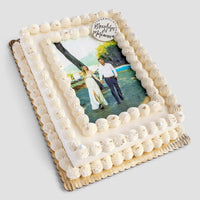 The Classic Sheet Cake by Jenna Rae Cakes features white frosting, piped borders, and an edible photo of a couple holding hands outdoors, finished with a small Congratulations plaque in the top corner.