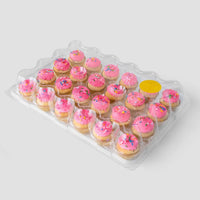 A clear plastic tray of 24 mini cupcakes with pink frosting and colorful sprinkles from Jenna Rae Cakes Dessert Tables line, featuring one empty slot covered by a yellow sticker, set against a plain light gray background.