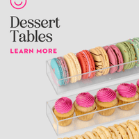 Clear trays of colorful macarons, pink frosted cupcakes, and cookies from Jenna Rae Cakes’ Dessert Tables are shown on a light background. “Dessert Tables, Learn More” appears below a smiley face logo.