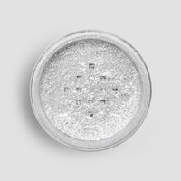 A round container of Jenna Rae Cakes Dazzle Dust Best Seller Trio is filled with fine, shimmery silver glitter powder, shown from above against a light gray background.