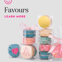 Colorful Jenna Rae Cakes Favours macaron gift boxes, some tied with pink ribbons, are stacked on a light background. A pink smiley logo appears above the text “Favours Learn More.”.