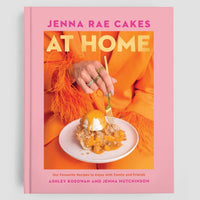 The Home Baker Bundle by Jenna Rae Cakes features a pink cookbook, Jenna Rae Cakes At Home, by Ashley Kosowan and Jenna Hutchinson, with a cover showing someone in orange cutting into a dessert topped with whipped cream and fruit.