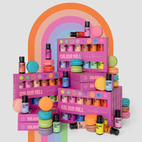The Jenna Rae Cakes x Colour Mill Pack by Jenna Rae Cakes is displayed alongside colorful macarons before a rainbow arch, featuring vibrant, playful energy and bright pink packaging on a light background.