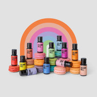 Jenna Rae Cakes x Colour Mill Pack bottles are displayed with pastel macarons in front of a vibrant rainbow arch, all set against a light grey background.