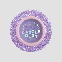 A package of six 5g shakers of Jenna Rae Cakes Lavender Haze Edible Glitter, each with a pink lid and iridescent label, sits among sparkling purple sugar crystals.