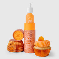 A bottle of Jenna Rae Cakes Liquid Candy Peach, featuring an orange label, is placed by its box, two stacked orange cupcake liners, and a peach-frosted cupcake with a small orange candy on a light backdrop.