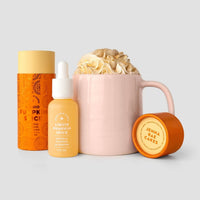 A pink mug with whipped cream sits next to a Jenna Rae Cakes Liquid Pumpkin Spice - Package of 6, an orange container, and a tin—all set against a light gray background.