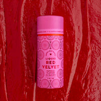A package of 6 Jenna Rae Cakes Liquid Red Velvet bottles sits on a textured red surface, resembling cake batter or frosting, with decorative patterns and text on the pink labels.