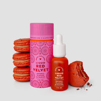 A stack of red macarons sits beside a pink bottle and a dropper bottle labeled Jenna Rae Cakes Liquid Red Velvet - Package of 6 Natural Flavour for Baking. One macaron is bitten, revealing its red interior, with a light gray background.