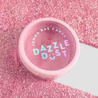 A small pink container labeled Jenna Rae Cakes Lollipop Edible Glitter - 5g Shaker (Package of 6) sits on a sparkling pink glitter surface, with white and iridescent text standing out on the lid.