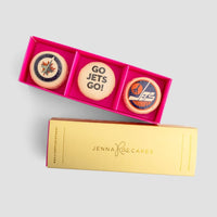 The Macaron Message Gift Box by Jenna Rae Cakes features three macarons in a pink box—two with Winnipeg Jets logos and one with GO JETS GO!—displayed beside a yellow Jenna Rae Cakes sleeve.