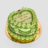 The Olive Martini Heart Cake by Jenna Rae Cakes features green icing, gold pearls, a cherry on top, and a little one is on the way in gold lettering. Shaped like a heart, this cake is presented on a gold board.