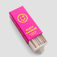 A bright pink Jenna Rae Cakes Party Candles box with a yellow smiley face and 20 beeswax candles displays cream-colored candles, some visible through the open end, set against a light gray background.