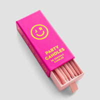 A partially open pink box labeled Party Candles by Jenna Rae Cakes with yellow text and smiley face graphics reveals several pink beeswax candles inside.