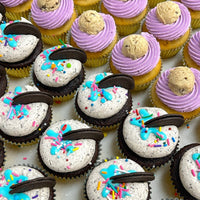 Rows of Jenna Rae Cakes Regular Cupcakes: chocolate with white frosting, blue drizzle, sprinkles, Oreo pieces, and vanilla with purple frosting topped with cookie dough balls.