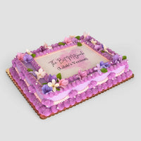 The Sugar Flower Sheet Cake by Jenna Rae Cakes is a rectangular cake with purple icing, pink and purple flowers, green leaves, and “The Past is Prologue (Gladia’s Version)” written in the center.