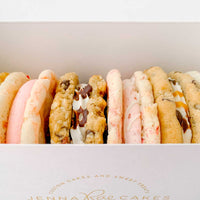 The Jenna Rae Cakes Cookie Sandwich Gift Box features a white box with the brands logo, filled with assorted cookie sandwiches in various flavors and colors, some cream-filled or drizzled with chocolate.