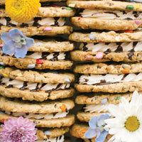 Regular Cookie Sandwiches by Jenna Rae Cakes are oatmeal cookies with colorful candies, white cream filling, and a chocolate drizzle, finished with fresh flowers like daisies and pink or blue blossoms.