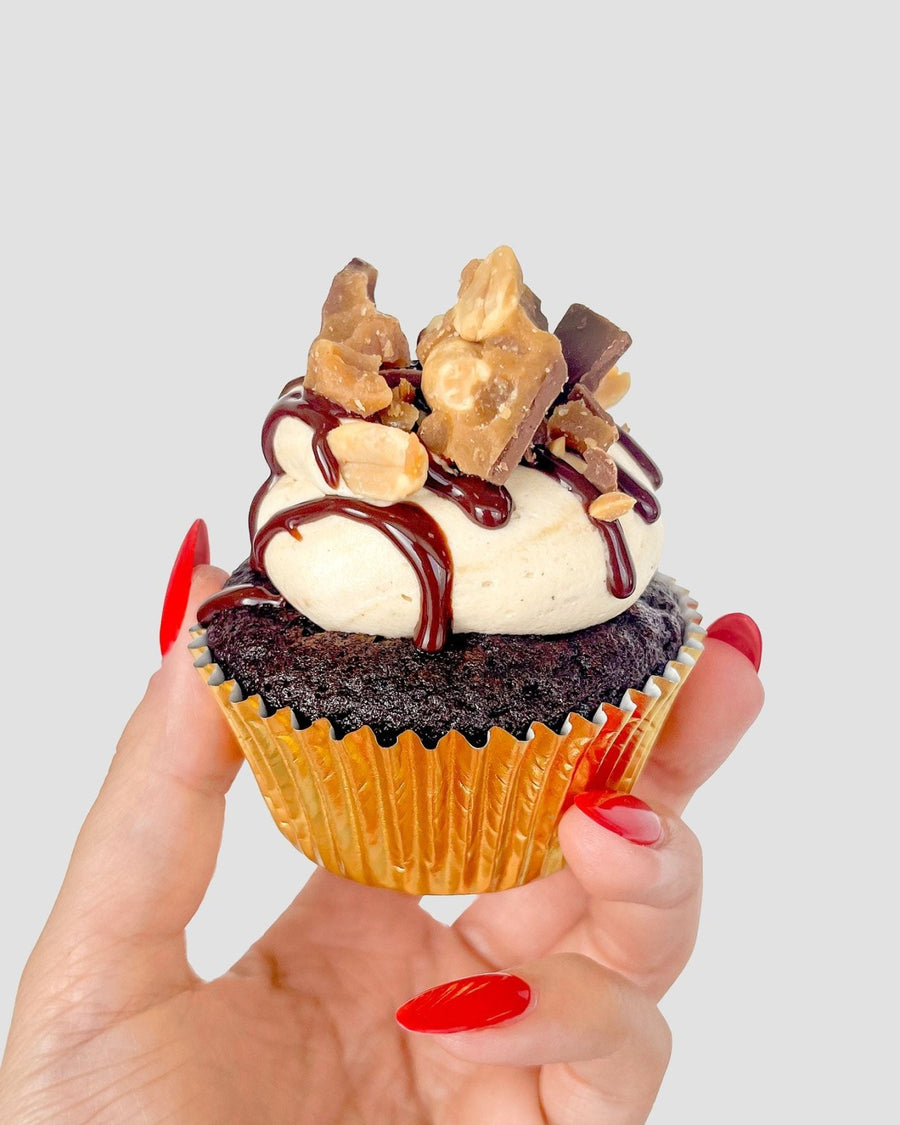 A hand with long red nails holds the $100 JRC Gift Bag from Jenna Rae Cakes against a plain light grey background.