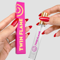 A person with red manicured nails holds a pink and yellow $165 JRC Gift Bag box by Jenna Rae Cakes in one hand and a clear bottle labeled $165 JRC Gift Bag in the other.