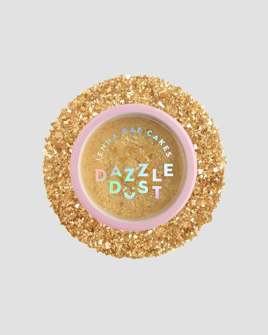 A round container of Jenna Rae Cakes FND TESTING - 24k Magic Edible Glitter (Copy), filled with gold edible glitter, is surrounded by loose gold glitter on a light grey background. The pink lid features colorful holographic text.