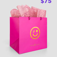The $75 JRC Gift Bag by Jenna Rae Cakes features a bright pink bag with a yellow smiley face and JR logo, pink tissue paper inside, and Jenna Rae Cakes written on the front. $75 is shown in purple text in the top right corner.