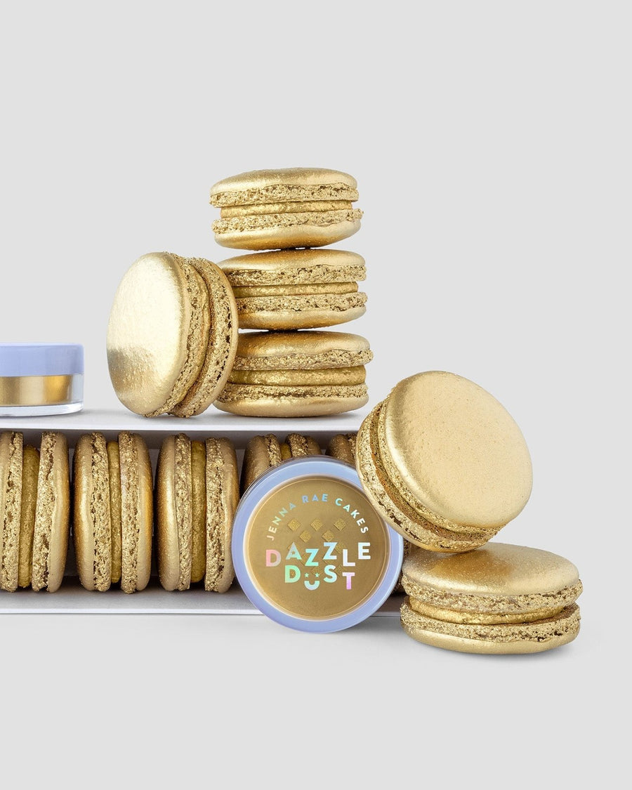 A set of golden macarons is displayed with a Jenna Rae Cakes Antique Gold Edible Lustre Dust (20g, pack of 3) in front, all on a simple light gray background.