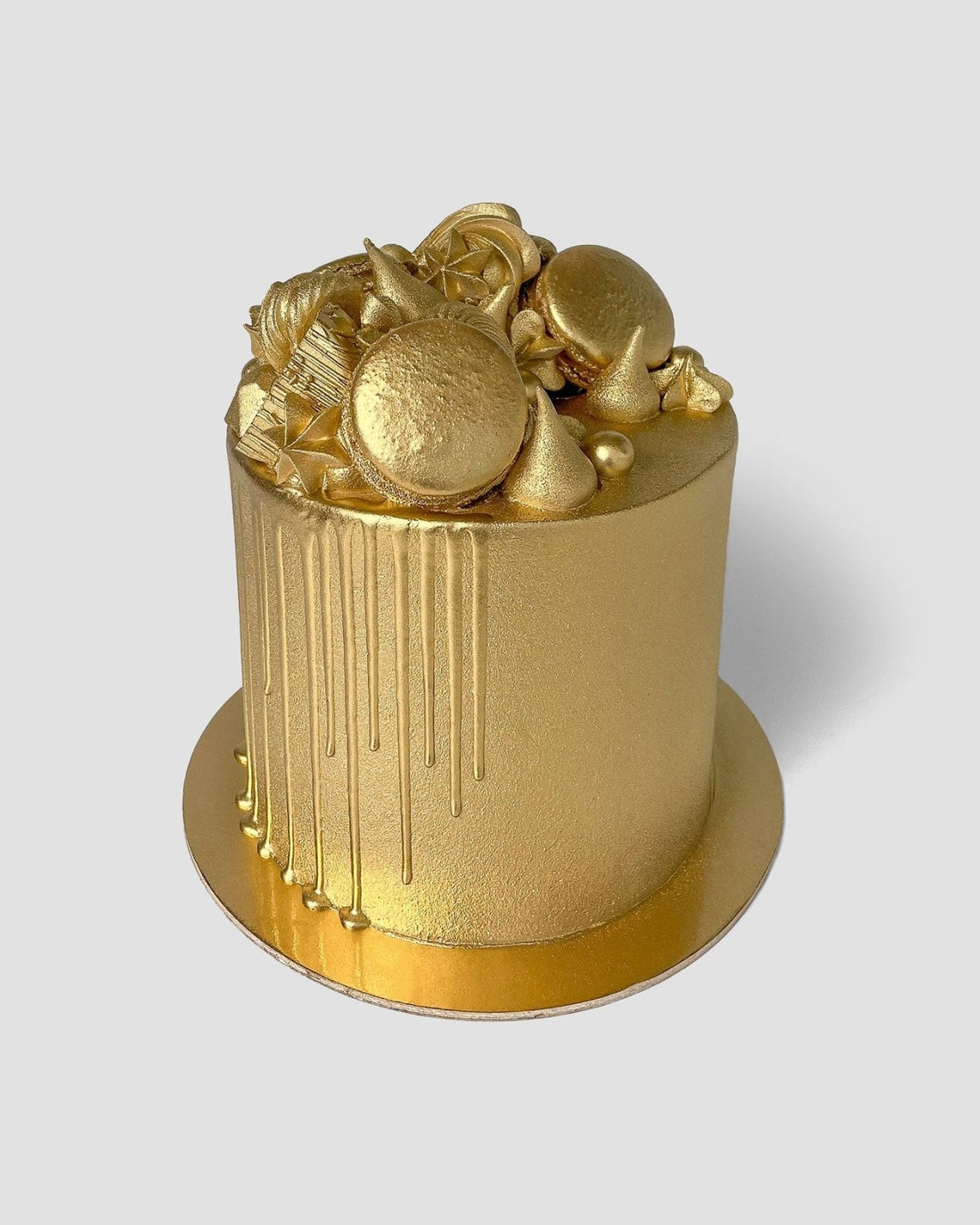A cake decorated with Jenna Rae Cakes’ Antique Gold Edible Lustre Dust (5g shaker, pack of 6): gold fondant, gold drip, assorted gold sweets and meringues on a gold board, set against a plain light background.