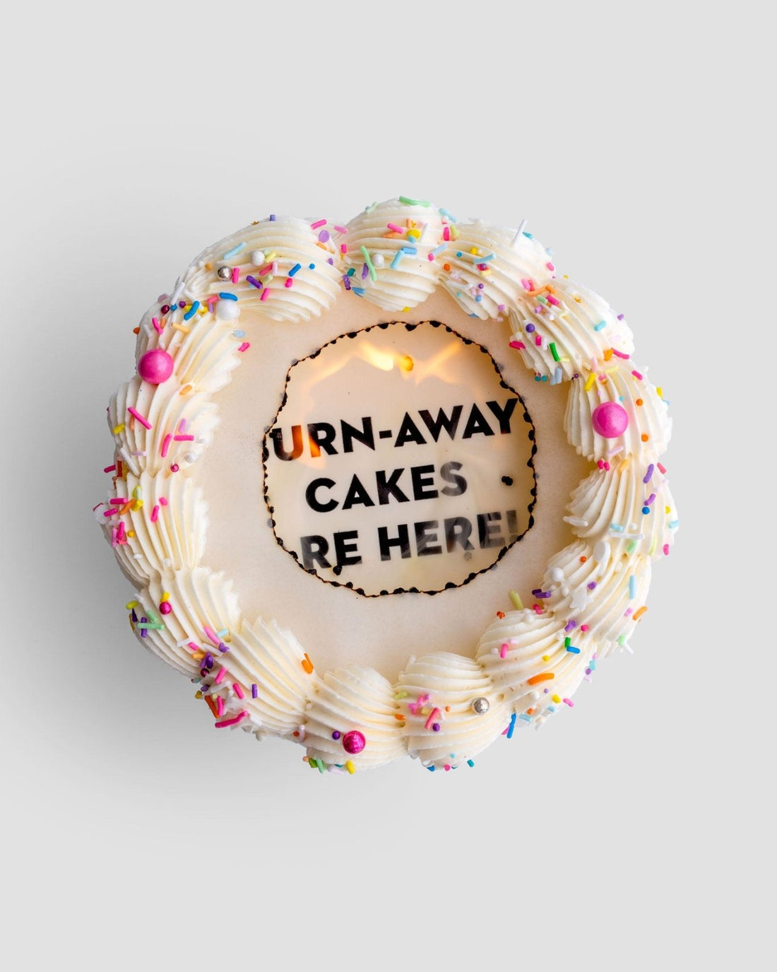 A round Burn Away Cake by Jenna Rae Cakes with white icing, colorful sprinkles, and pink and silver pearls. The center features a cutout revealing the hidden message: TURN-AWAY CAKES ARE HERE!.
