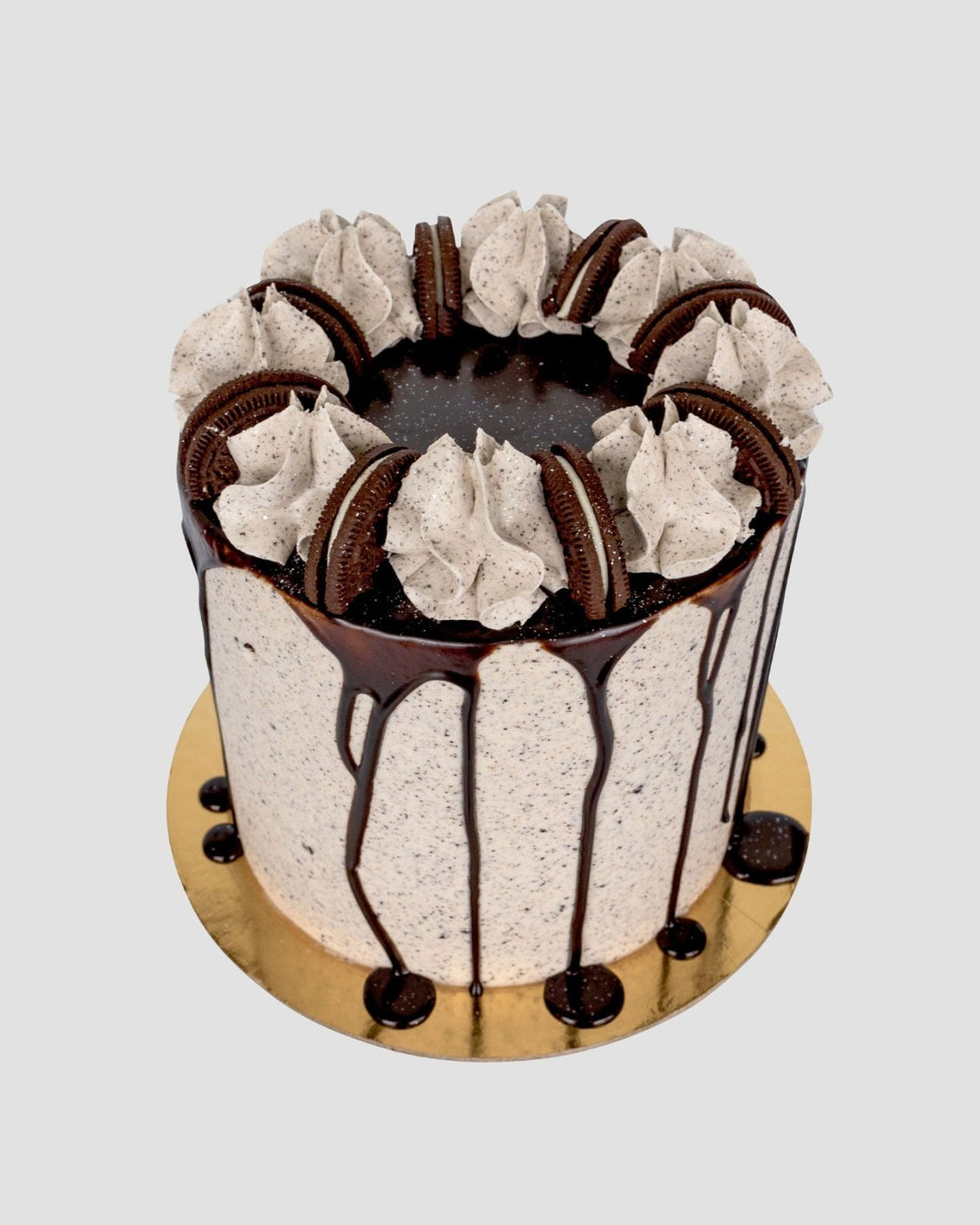 Jenna Rae Cakes’ Chocolate Oreo Cake features layers of cookies and cream, chocolate drip icing, swirls of cream, and Oreo halves, beautifully presented on a gold cake board.