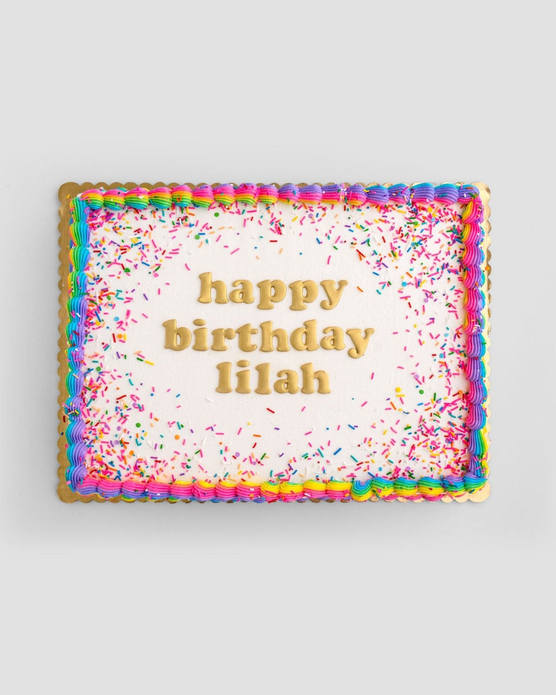 Jenna Rae Cakes Classic Sheet Cake features white icing, rainbow borders, colorful sprinkles, and happy birthday lilah written in yellow letters.