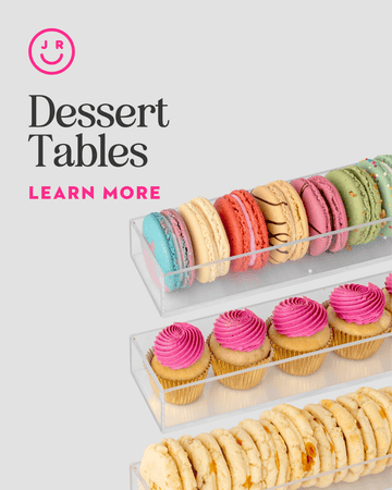 Clear trays of colorful macarons, pink frosted cupcakes, and cookies from Jenna Rae Cakes’ Dessert Tables are shown on a light background. “Dessert Tables, Learn More” appears below a smiley face logo.