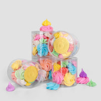 Jenna Rae Cakes Favours: Clear plastic jars filled with colorful meringue cookies in yellow, pink, blue, purple, and green are stacked on a light gray background, with some meringues scattered around.