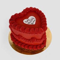 The Heart Cake by Jenna Rae Cakes is a heart-shaped red cake with decorative red frosting and a white heart on top reading talk strictly to me, presented on a round gold cake board.