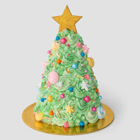 A cake decorated to look like a Christmas tree with green frosting, colorful candies, and meringues, topped with a large gold star, displayed on a gold cake board against a plain background.