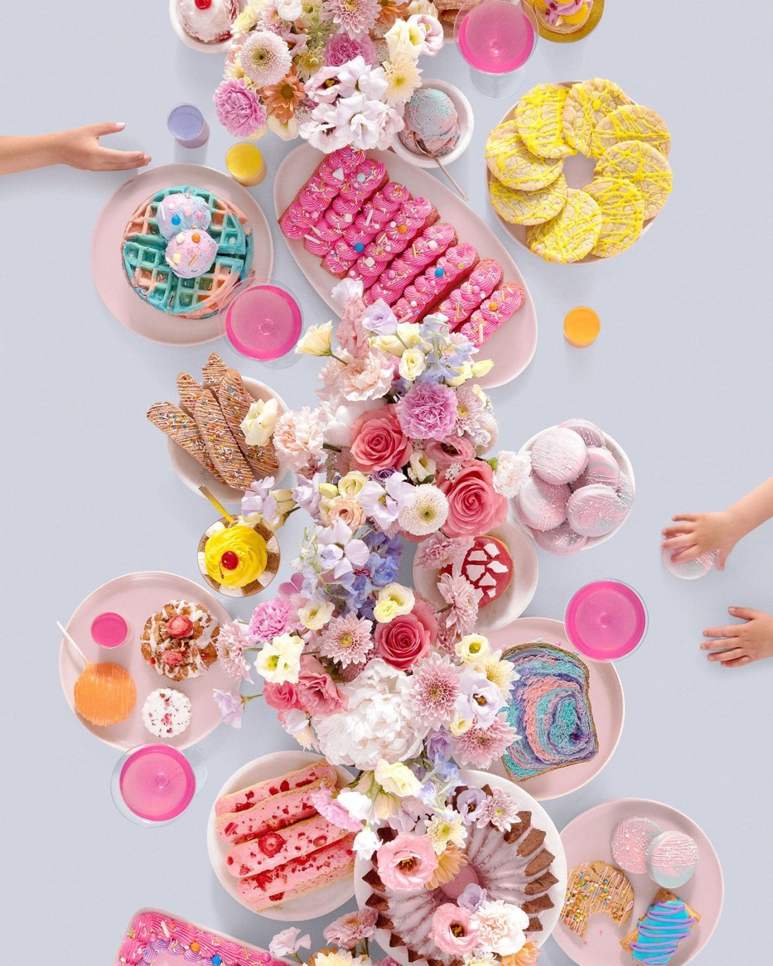 A festive dessert table inspired by Jenna Rae Cakes at Home Cookbook displays pink plates, colorful pastries, waffles, and macarons as children reach for treats. The bright scene captures the playful spirit of Jenna Rae Cakes.