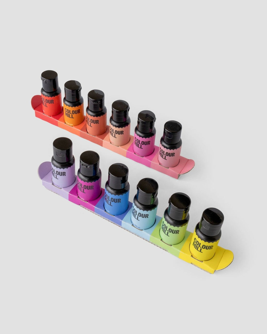 The Jenna Rae Cakes x Colour Mill Pack by Jenna Rae Cakes features ten food coloring bottles in assorted colors, arranged in two rows on rainbow-gradient cardboard trays against a light gray background.