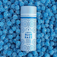 A bottle of Jenna Rae Cakes Liquid Blue Razz stands upright on a layer of small, round, blue sugar-coated candies, creating a vibrant blue-themed background.