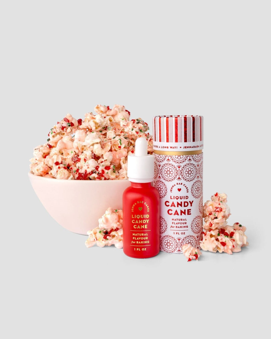 A bowl of popcorn with red and green sprinkles sits beside a striped container and a red bottle of Jenna Rae Cakes Liquid Candy Cane - Package of 6, all on a light gray background.
