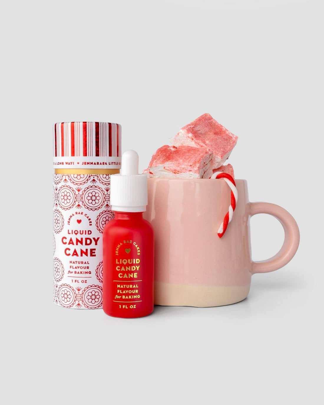 A pink mug with marshmallows, a candy cane, and Jenna Rae Cakes Liquid Candy Cane - Package of 6 with dropper and matching container are displayed against a light gray background.