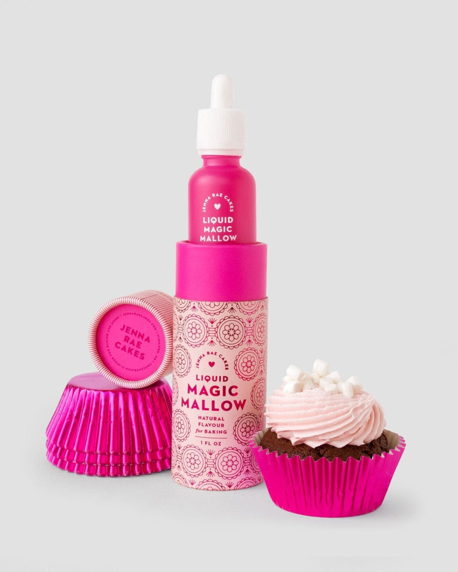 A package of 6 Jenna Rae Cakes Liquid Magic Mallow bottles stands upright next to pink cupcake liners, a pink lid labeled Jenna Rae Cakes, and a chocolate cupcake topped with pink frosting and mini marshmallows.