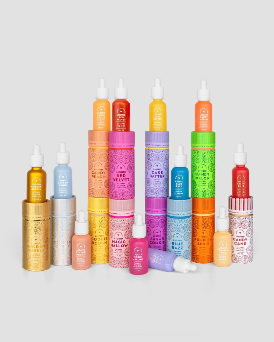 A vibrant row of Jenna Rae Cakes’ Liquid Pumpkin Spice serum bottles with matching decorative tubes is displayed on a light gray background. Each set features unique colors and labels for different scents or formulas.