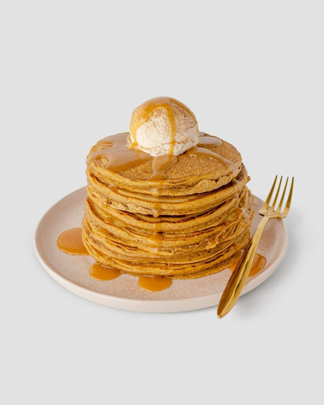 A light plate holds pancakes topped with ice cream and Jenna Rae Cakes’ Liquid Pumpkin Spice (package of 6), drizzled as syrup, beside a gold fork on a plain light background.