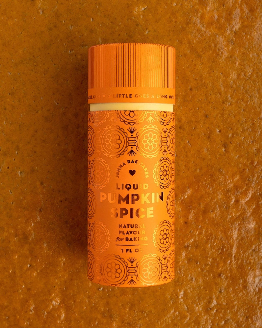 A small orange bottle of Jenna Rae Cakes Liquid Pumpkin Spice (Package of 6) with decorative patterns stands upright on a textured orange surface.