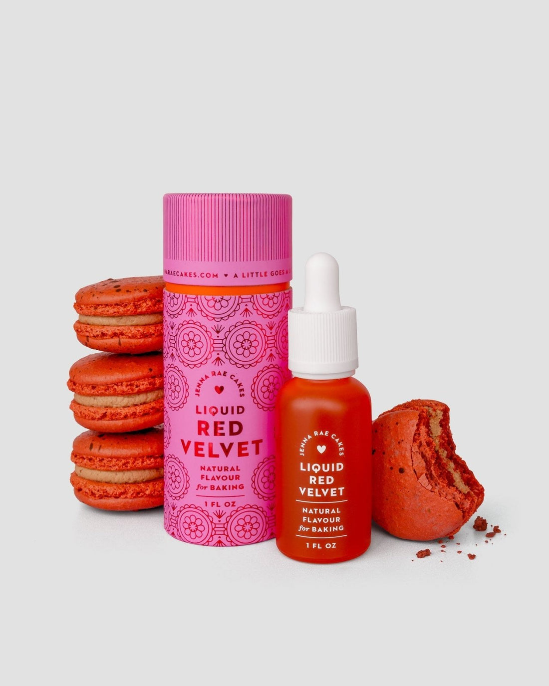 A stack of red macarons sits beside a pink bottle and a dropper bottle labeled Jenna Rae Cakes Liquid Red Velvet - Package of 6 Natural Flavour for Baking. One macaron is bitten, revealing its red interior, with a light gray background.