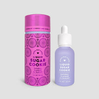 A Jenna Rae Cakes Liquid Sugar Cookie package of 6 is shown, featuring two bottles—one in a pink cylindrical container and one in a clear dropper bottle with decorative labels—displayed on a light grey background.