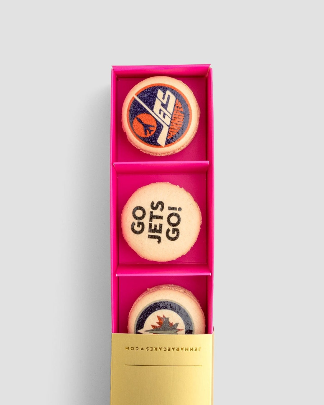 The Macaron Message Gift Box by Jenna Rae Cakes features three cookies in a pink box: one with a blue and orange logo, one with GO JETS GO!, and one with a blue, red, and white jet-themed logo.
