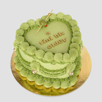 The Olive Martini Heart Cake by Jenna Rae Cakes features a heart-shaped green design with piped frosting, a green olive on a cocktail stick, golden pearls, and “a tini bit older” in gold letters atop a gold board.